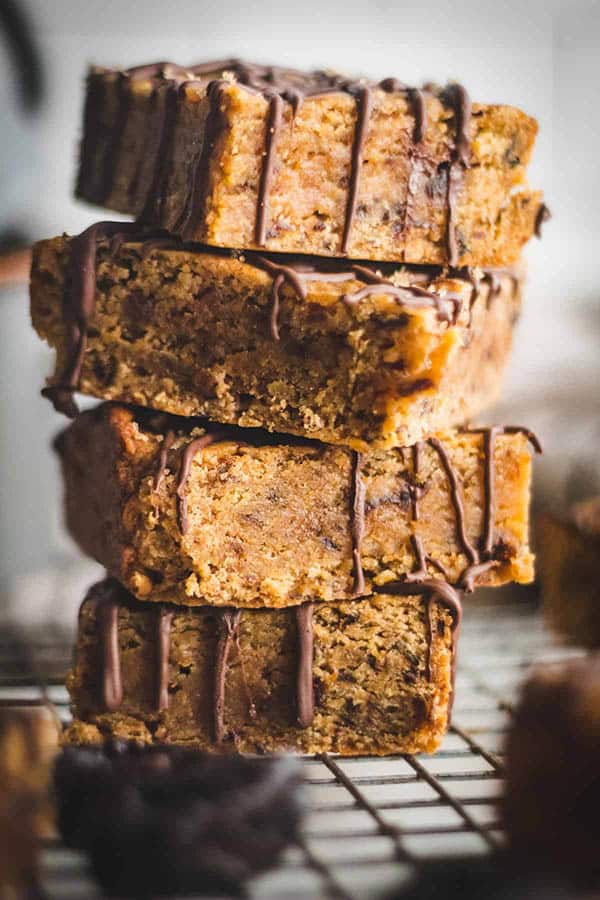 A stack of Miso Prune Blondies with chocolate drizzled over the top.