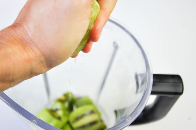 Kiwi's in a blender and person squeezing lime juice in blender