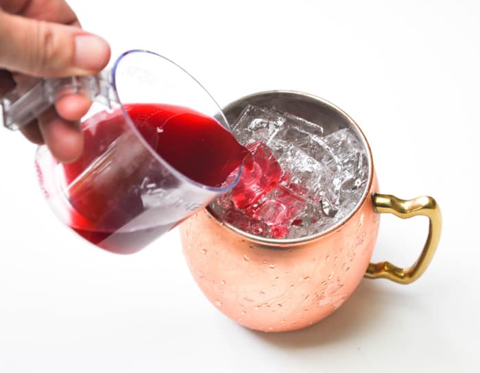 Pouring pomegranate juice over ice in copper mug