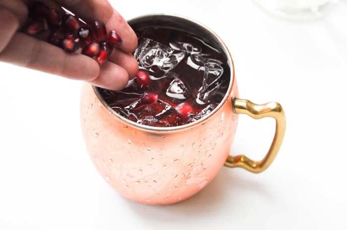 Adding fresh pomegranates into mug to top off drink