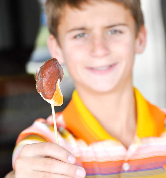 A child holding the chocolate covered tangerine on a skewer stick. 