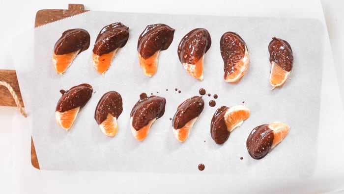 Half dark chocolate covered tangerines with sea salt sprinkled over on baking sheet