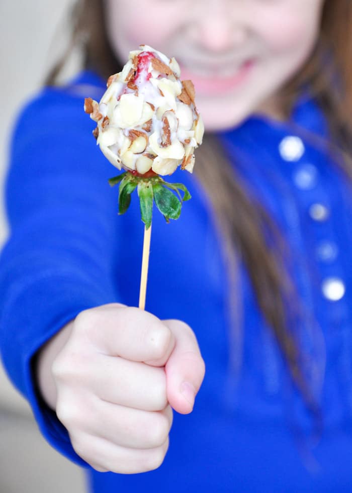 Child holding almond crusted strawberry of skewer 