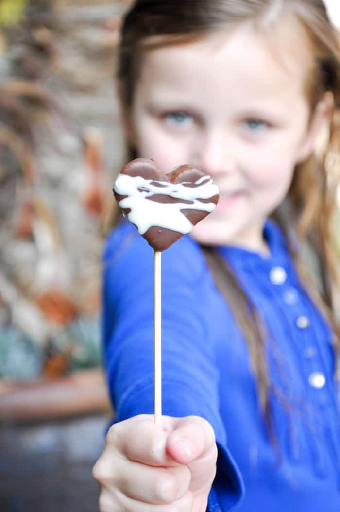 Child holding chocolate covered kiwi heart on skewer