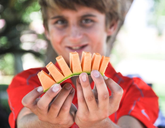 Child holding a slice of cut up cantaloupe 