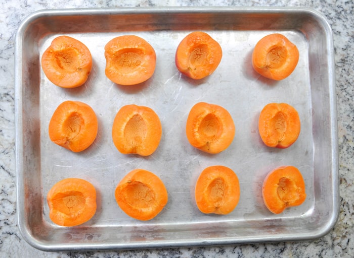 Sliced, pitted, and halved apricots on baking sheet