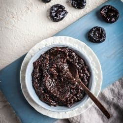 A bowl of prune puree with prunes scattered next to it.