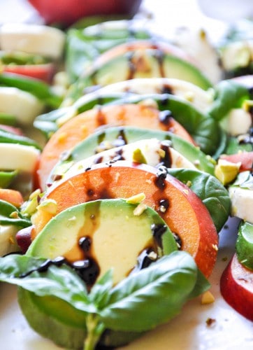 Thick rounds of avocado, nectarine and mozzarella are layered on a plate with basil sprigs before being drizzled in a balsamic reductjion and chopped pistachios. 