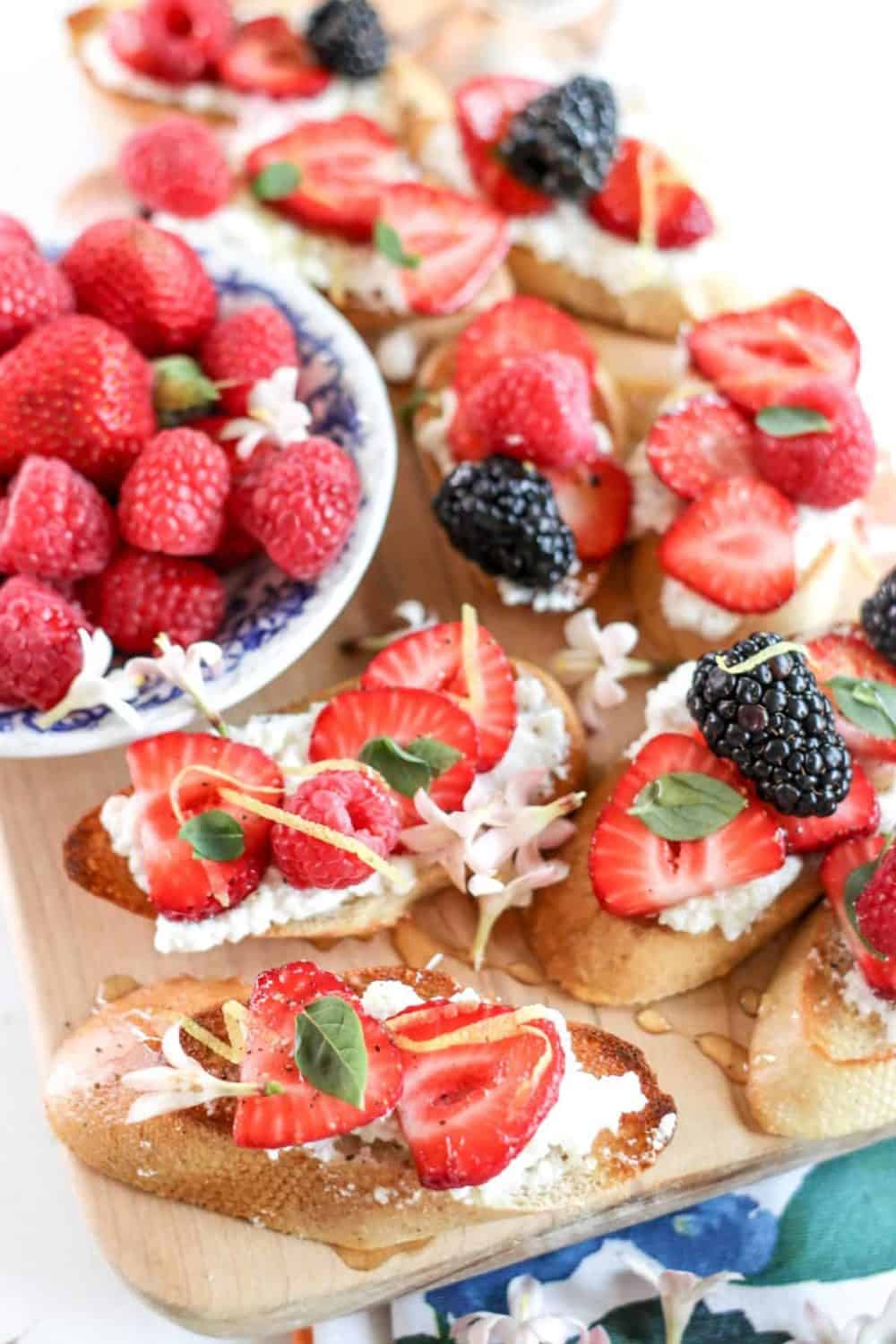 berry crostini on a board with a bowl of berries