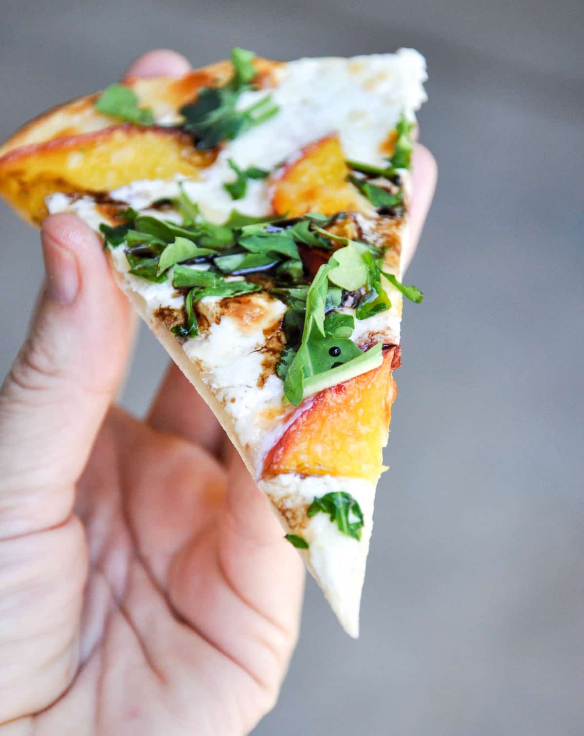 Person holding a slice of Nectarine Arugula Pizza