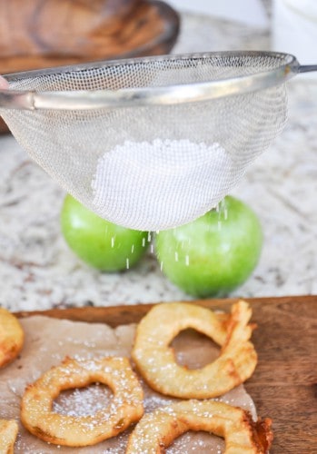 Powdered sugar being sprinkled over fried apple rings