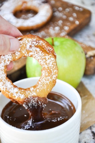 A fried apple ring being dunked in dipping sauce.