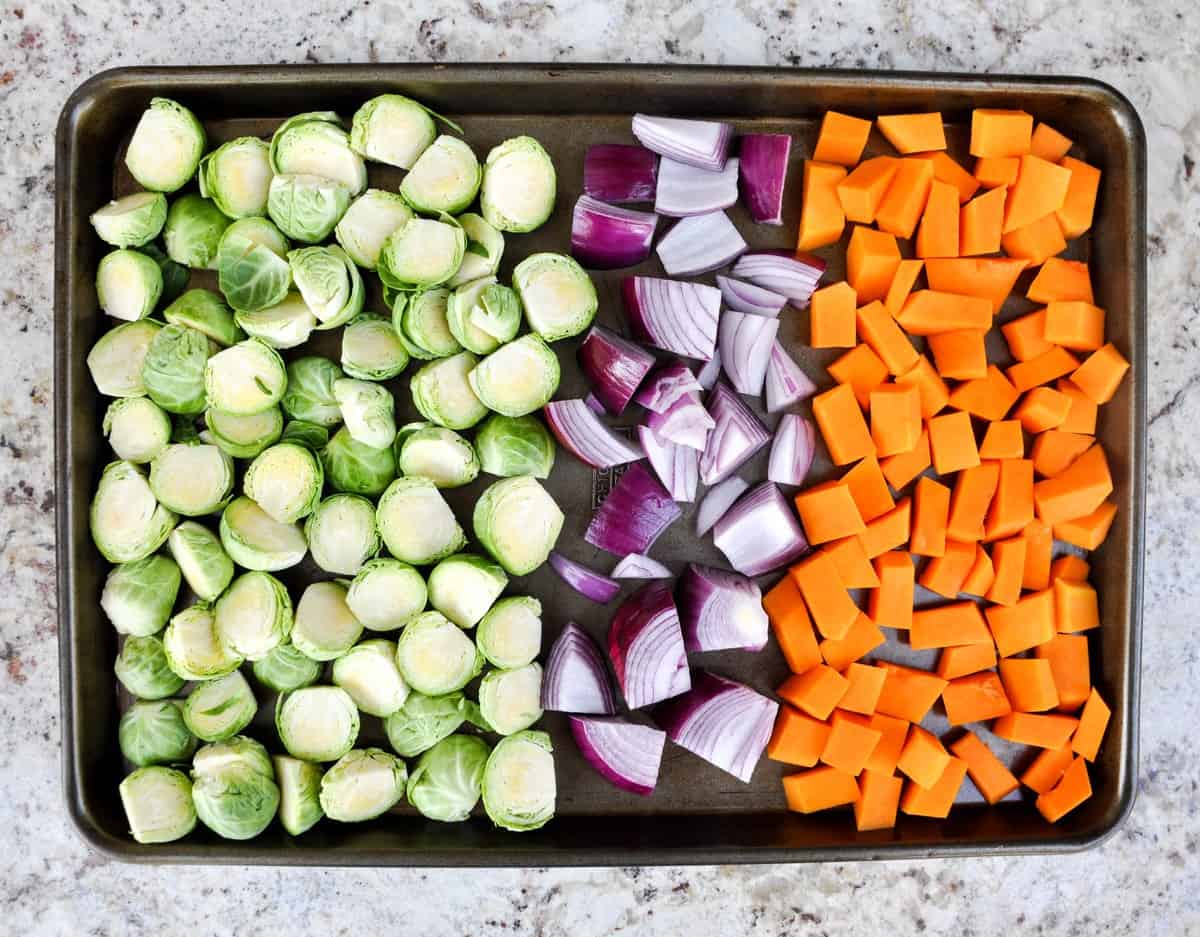 Ingredients chopped on a baking sheet: Brussels sprouts, red onion, and butternut squash 