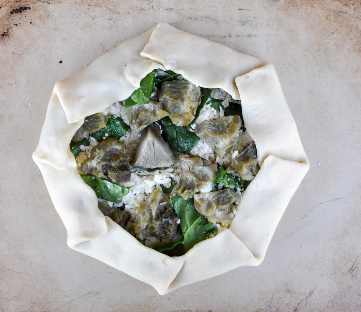 Edges of pie crust folded around Artichoke Spinach Galette ingredients 