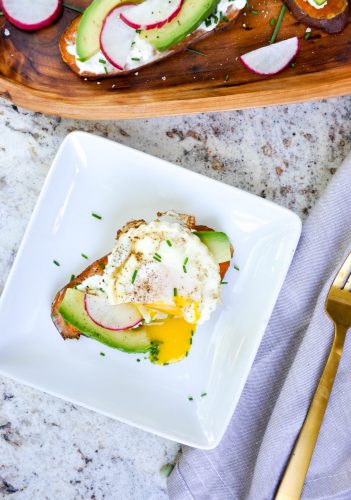 A thick slice of cooked sweet potato placed on a plate like a piece of toast then topped with avocado slices and an over easy egg. 