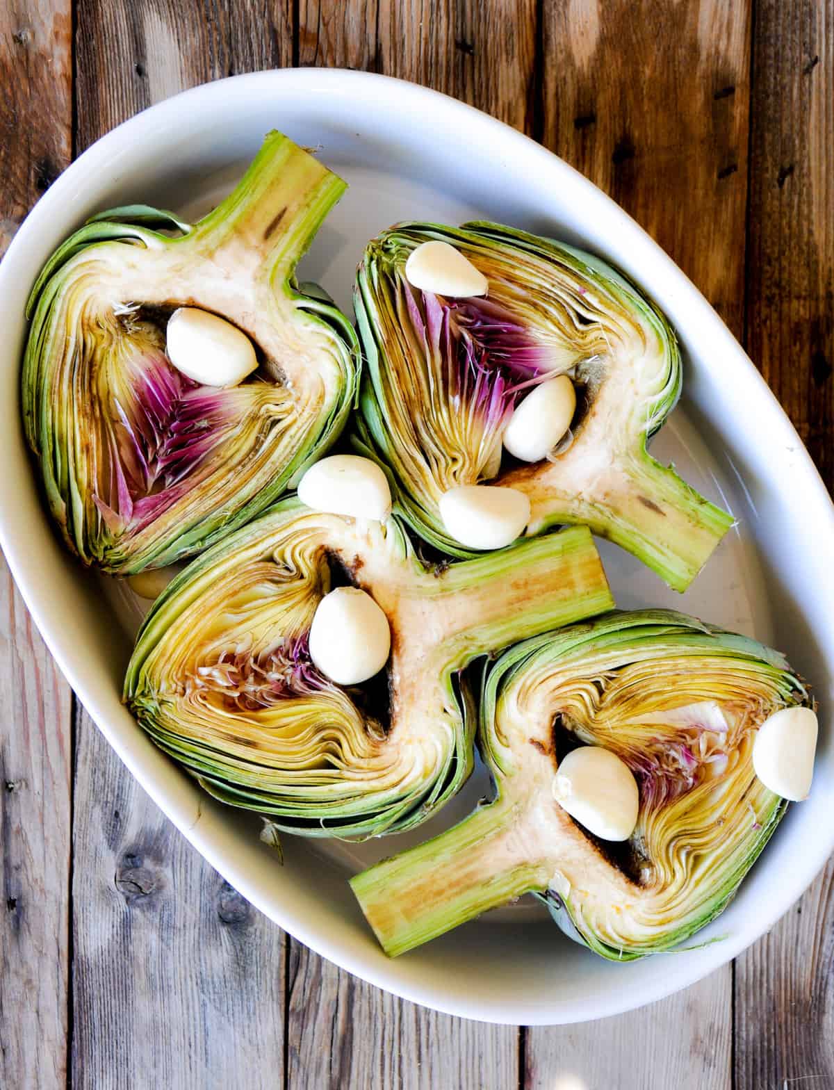 place artichoke halved side up in a baking pan with garlic cloves