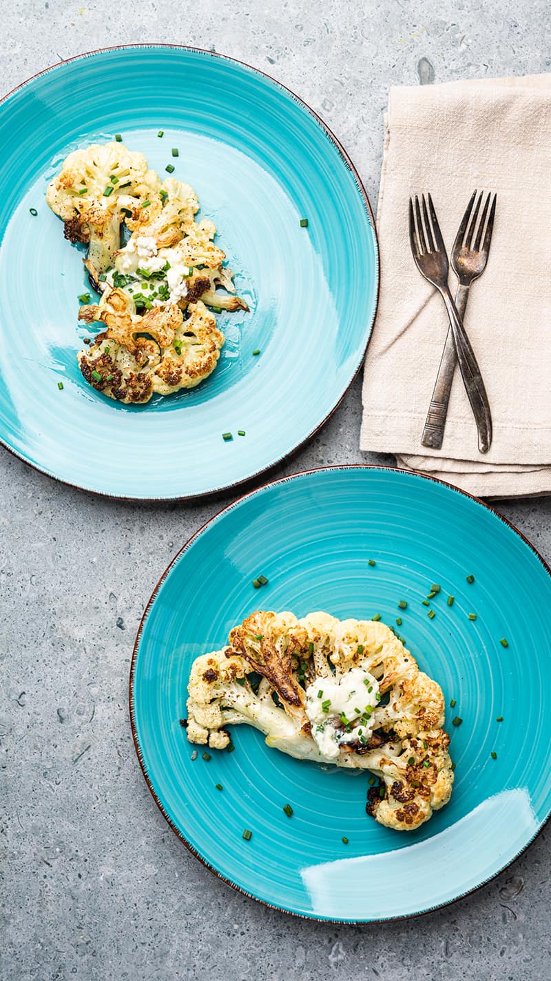 Two plates with cauliflower steaks topped in blue cheese butter.