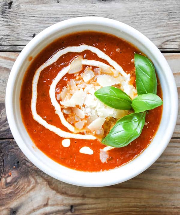 roasted tomato soup in bowl topped with cheese and basil.