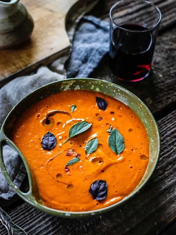 A bowl of blended tomato soup topped with an olive oil drizzle and basil leaves.