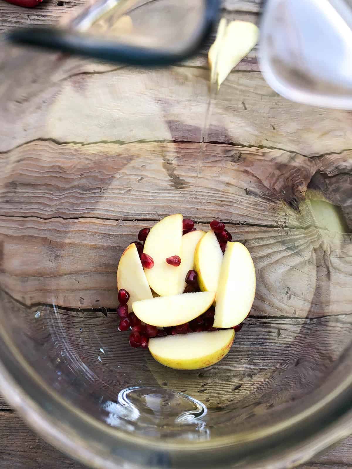 Simply add the sliced apples and pomegranate arils to the bottom of a glass pitcher.