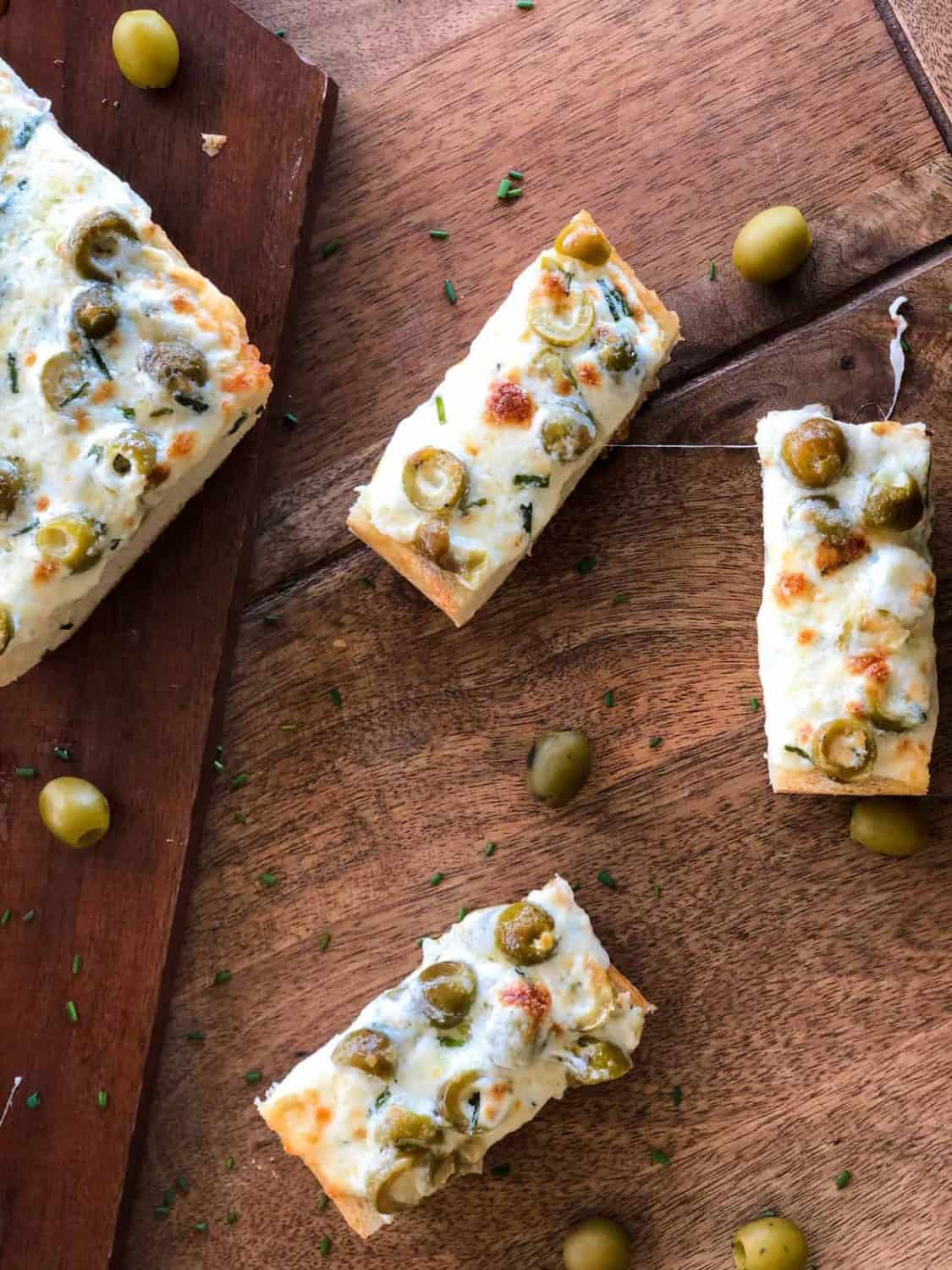 Green Olive Garlic Cheese Bread pieces are sliced on a wood table.