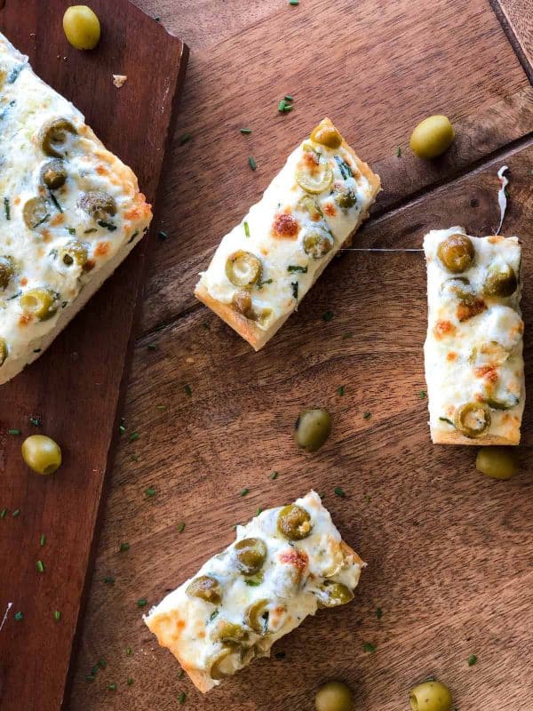 Green Olive Garlic Cheese Bread pieces are sliced on a wood table. 