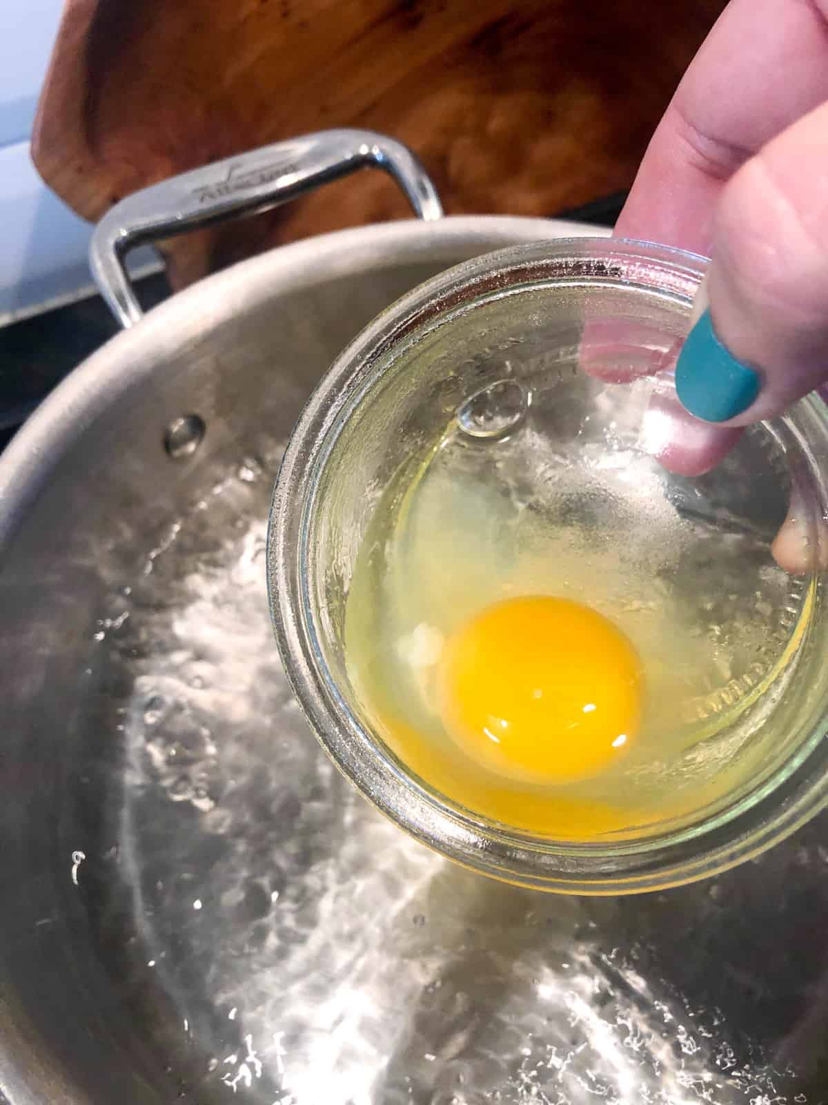 Add the egg into a small bowl and slide the egg into the water, keeping the bowl as close to the water as possible allowing the egg to go in all at once.