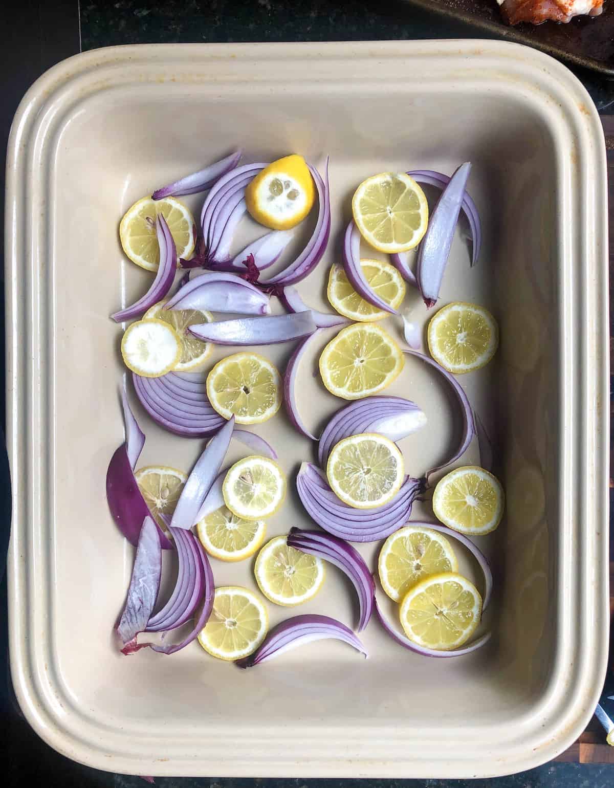 take a large pan and add sliced lemons and red onion to the bottom in a single layer.