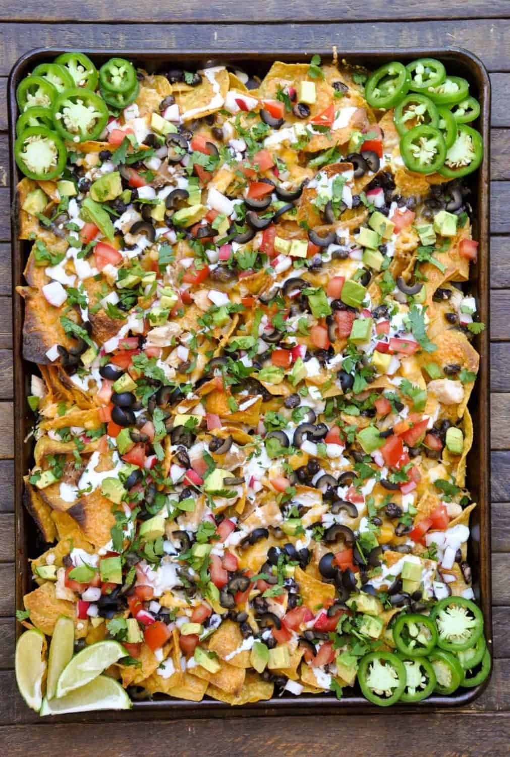 A Mexican inspired  sheet pan chicken recipe! A sheet pan full of nachos topped with chicken and fresh vegetables like avocado, tomato, onion, and cilantro. 