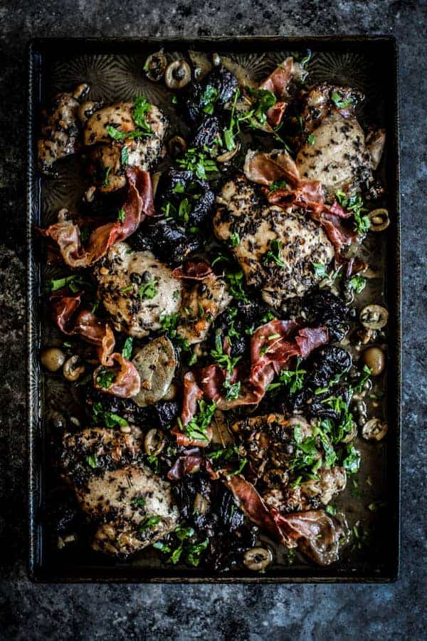 A sheet pan dinner with chicken thighs, green olives, prunes, and capers. 