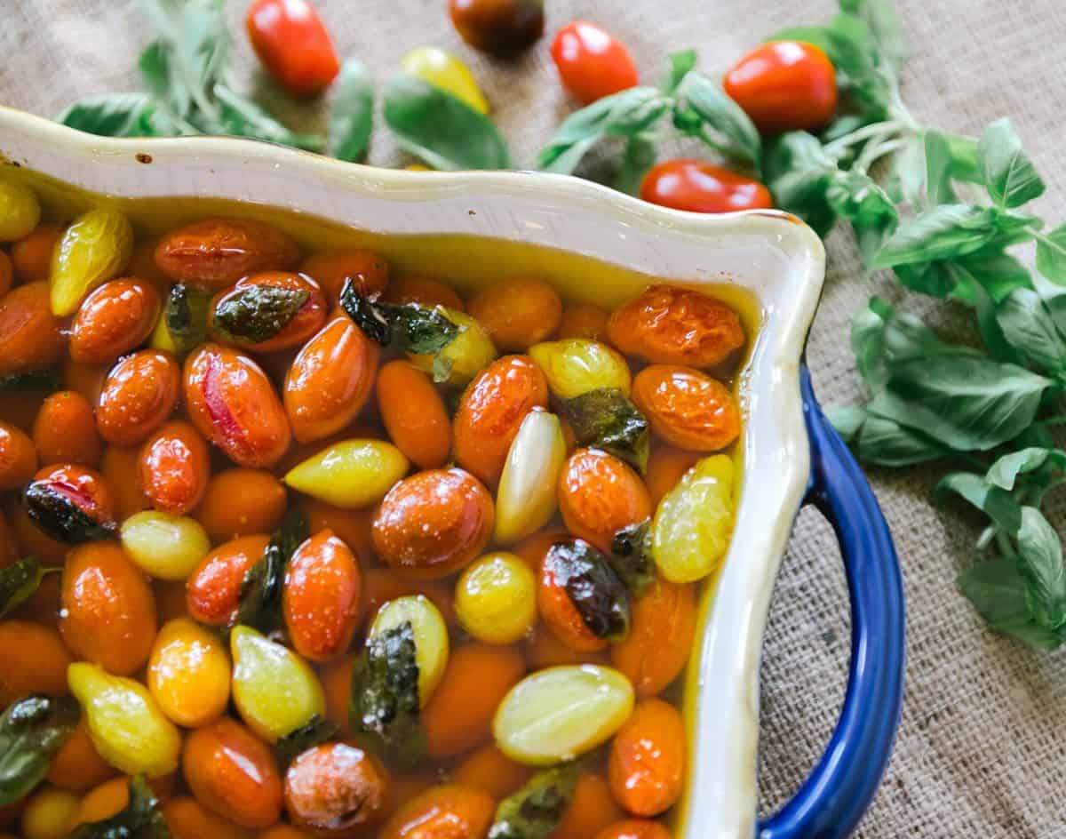 A close up of Tomato confit in a baking dish. Colorful cherry tomatoes and basil in olive oil. 