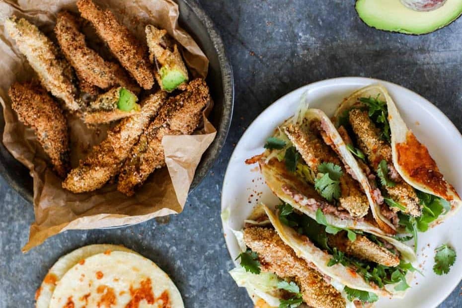 Crispy Avocado Tacos prepared on a serving plate next to a platter of crispy fried avocado spears.