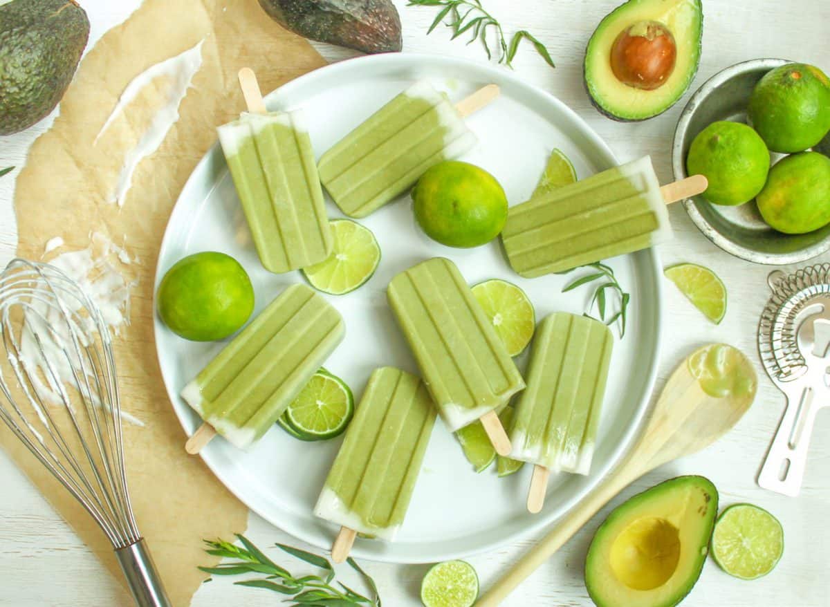 Looking down at a platter of green Tropical Avocado Popsicles. There are avocado and lime halves on the table as well. 
