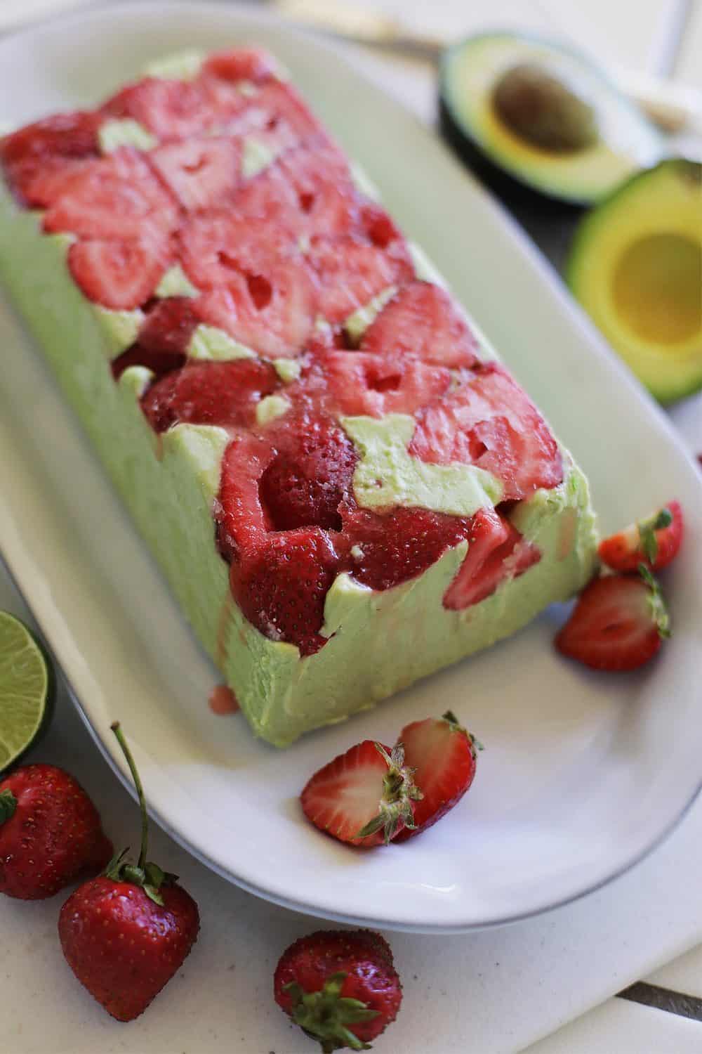 A top down look at an Avocado Coconut Strawberry Semifreddo. the semifreddo is green in color and has whole red raspberries frozen into the top .