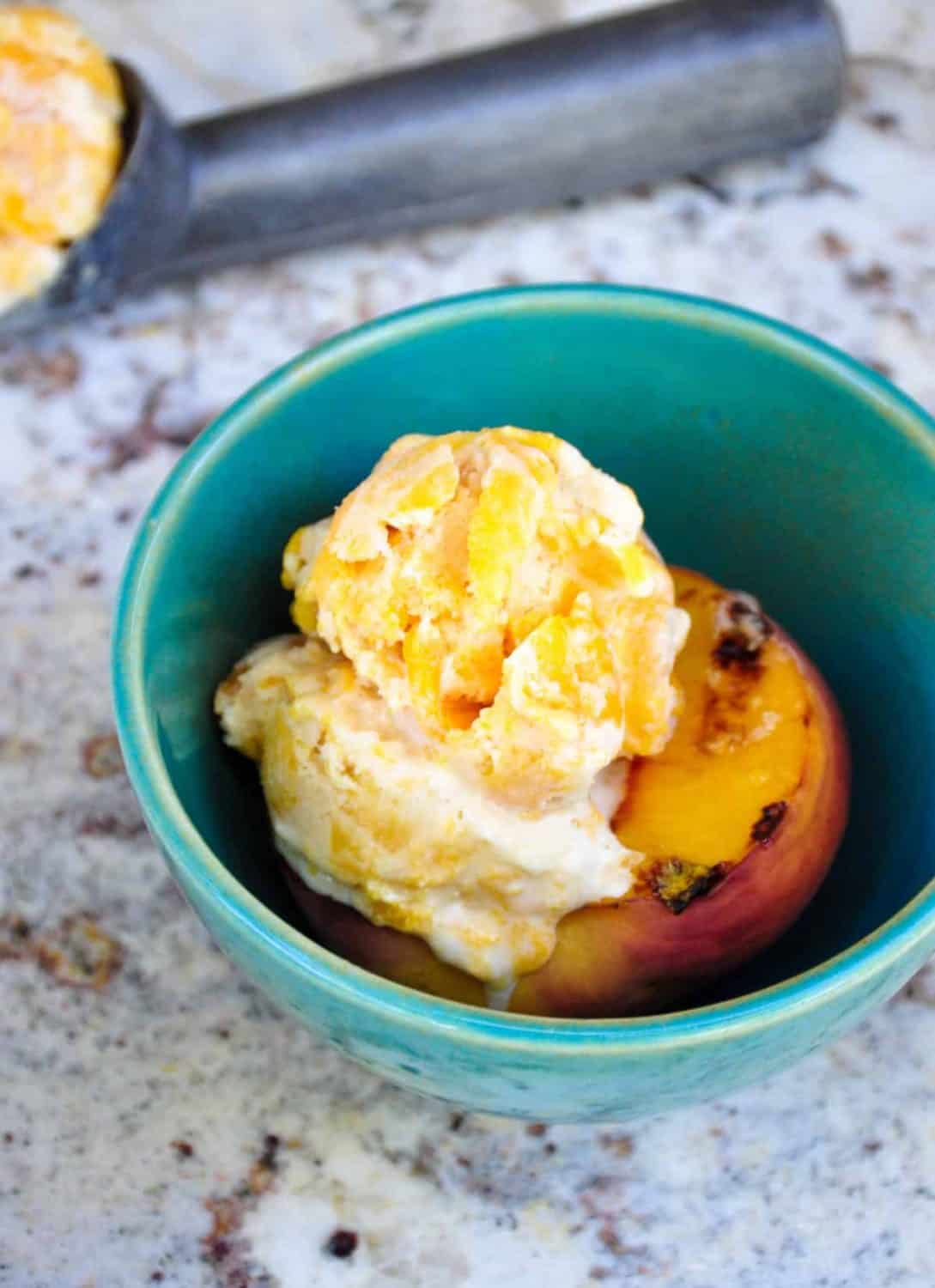 A bowl with a grille peach half in teh bottom and a scoop of peach ice cream on top.