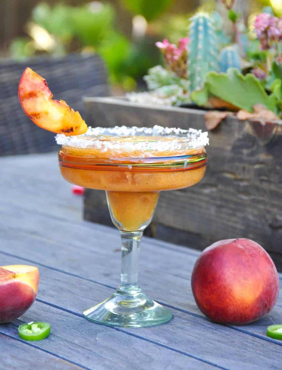 A margarita in a tall margarita serving glass with a grilled peach as a garnish.