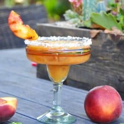 A margarita in a tall margarita serving glass with a grilled peach as a garnish.