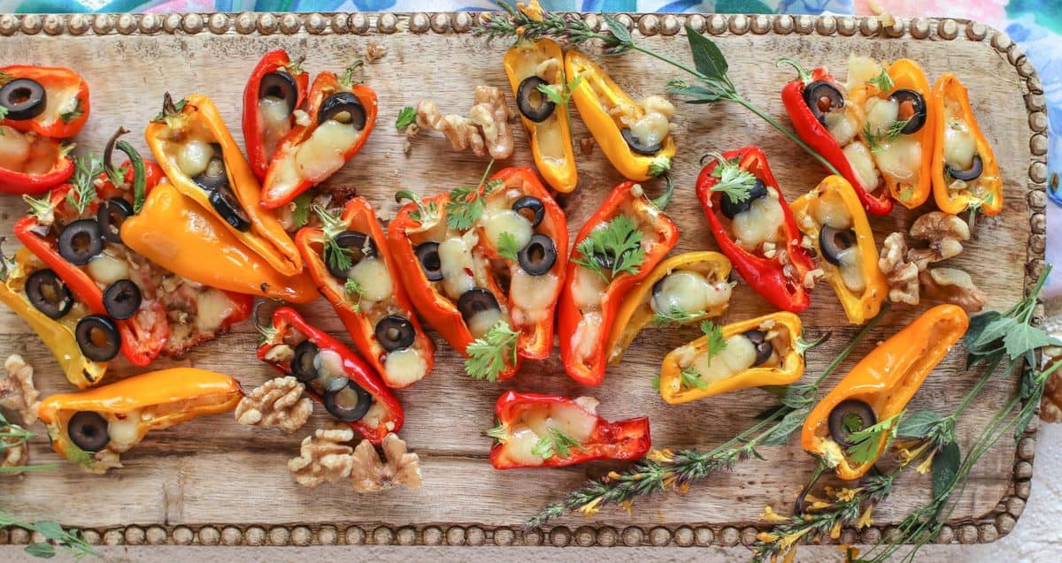 Mini stuffed peppers recipe. Colorful mini peppers are filled with thinly sliced black olives and melty jalapeño pepper jack cheese. Cilantro is scattered across the peppers.