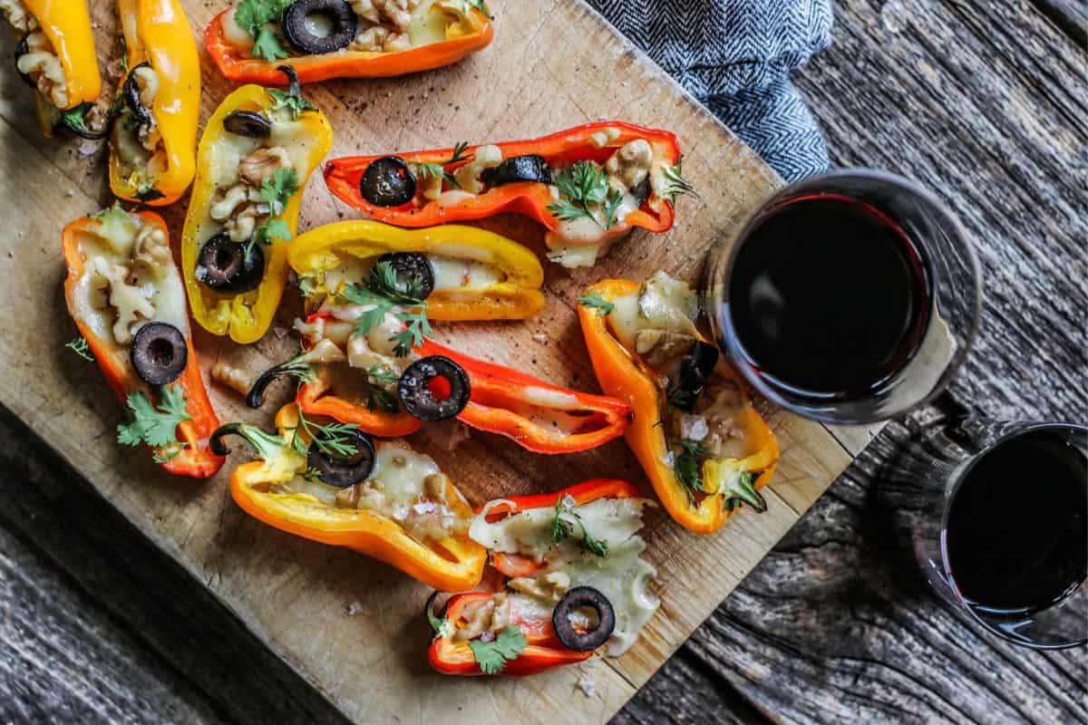 Mini Colorful Stuffed Peppers Recipe with Olives and Pepper Jack Cheese on a serving board with a stemless glass of red wine.
