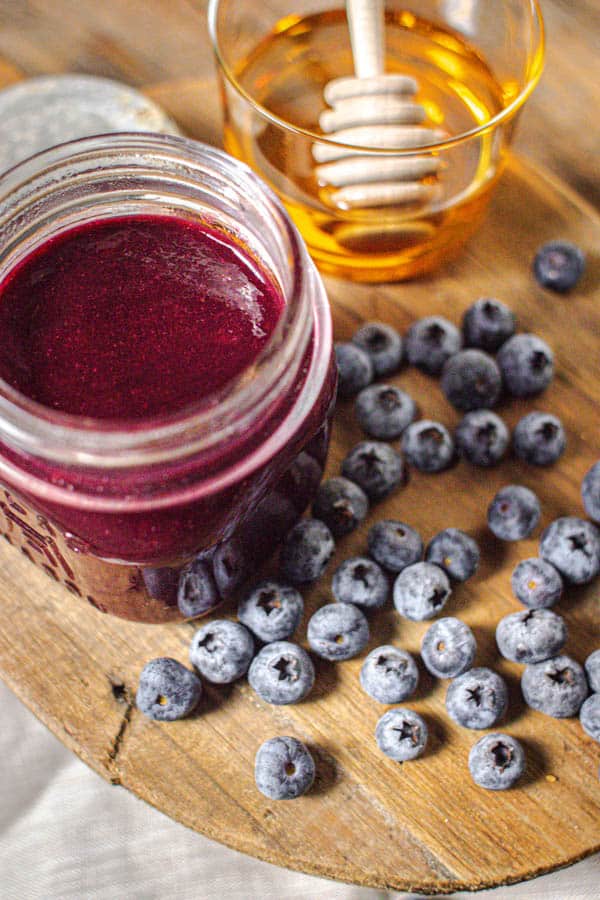 Blueberry Jalapeno BBQ sauce in a jar next to fresh blueberries and a small jar of honey.