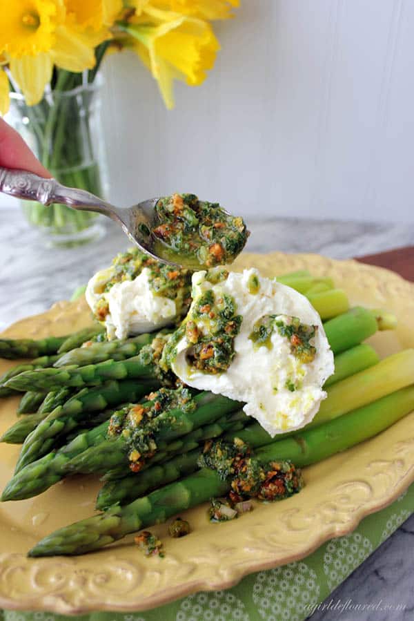 Blanched asparagus are topped with burrata and a pistachio salsa verde is being spooned over the top. Blanching is one of the best ways to cook asparagus.
