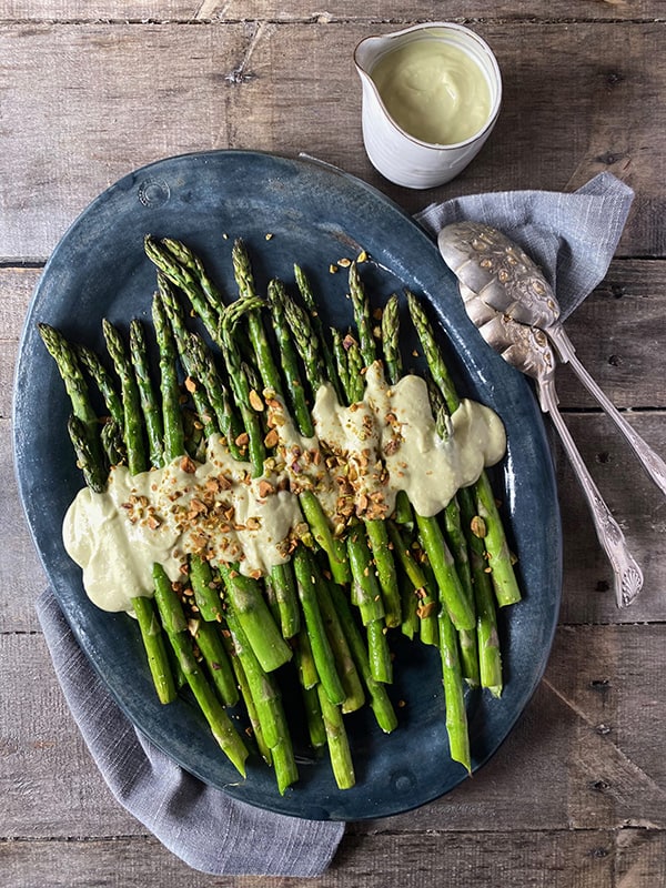 A platter of roasted asparagus topped with a garlic, tahini, and avocado dressing then sprinkled with crushed pistachios