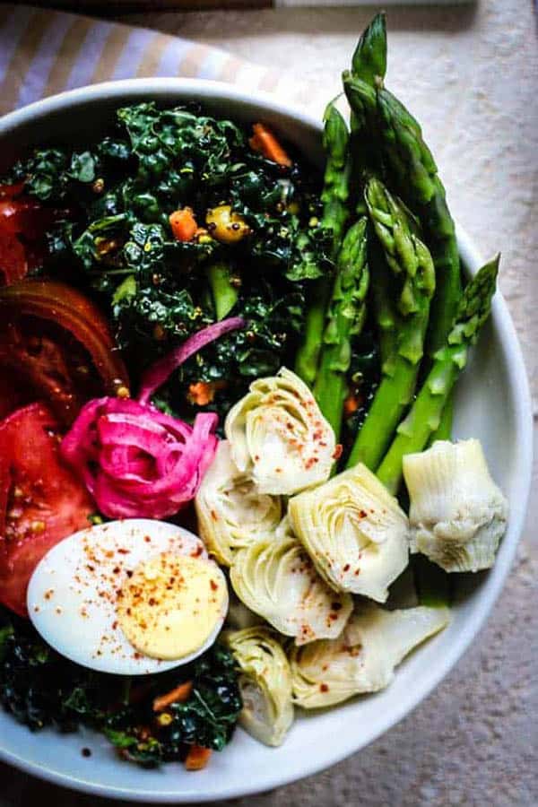 One of the best ways to cook asparagus is to blanche it. A bowl filled with kale and quinoa salad, blanched asparagus, hard boiled eggs, fresh tomatoes, and artichoke hearts.