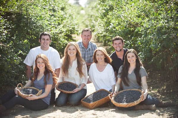 A farmer with his wife, 3 daughters, and 2 son in laws in a field of blueberry bushes holding baskets of fresh blueberries.
