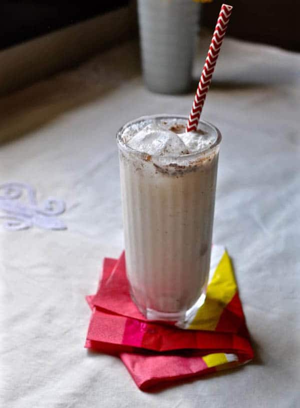 A glass of Almond-White Chocolate Horchata with a straw sitting on a cocktail napkin.
