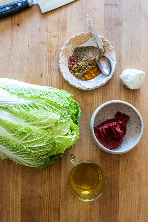 The ingredients needed to make this Napa cabbage recipe. A head of Napa cabbage, tomato paste, garlic, olive oil, and spices.