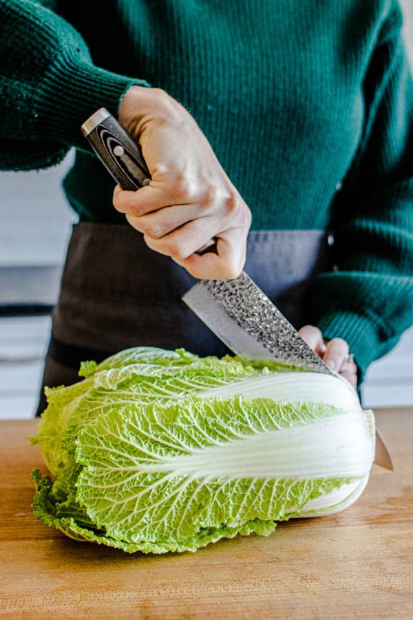 Breaking down a head of Napa cabbage by slicing it in half through the core towards the ends of teh leaves for our Melting Napa Cabbage recipe.