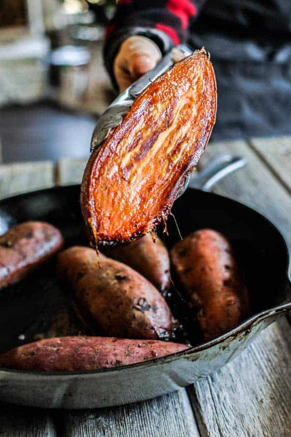 A roasted, halved sweet potato that was face down in a skillet has been picked up with tings showing the camera a perfectly golden caramelized exterior on the cut side.