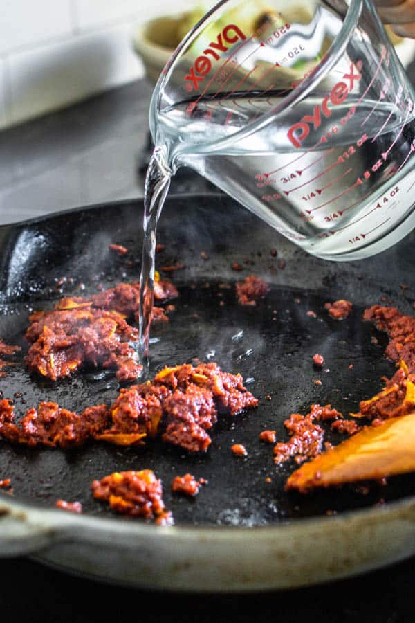 Water being added to the skillet with seasoned tomato paste for our Melting Napa Cabbage recipe.