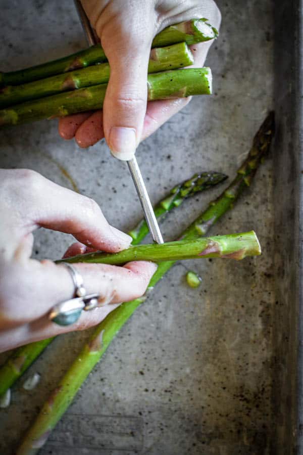 An asparagus spear being threaded onto a skewer for grilling. 